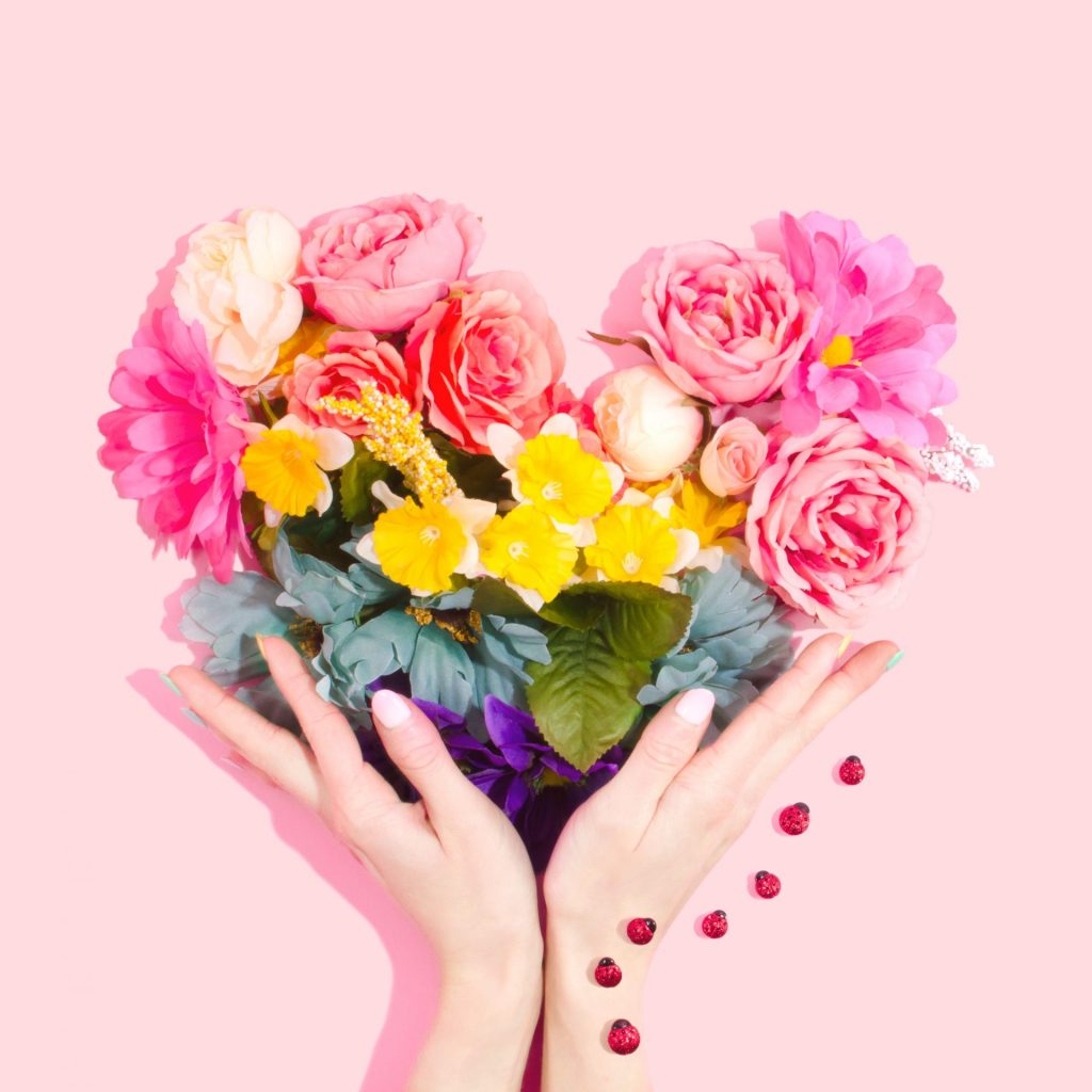 ręce i kwiaty ułożone w serce na różowym tle