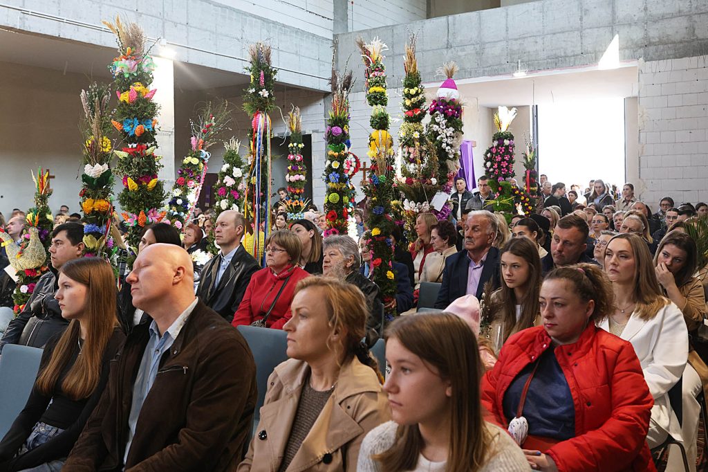 Na obrazku widoczni są ludzie siedzący w pomieszczeniu, które są ozdobione dodatkowymi aranżacjami. Atmosfera, która może być kulturalna lub religijna, obejmuje społeczność wokół tradycji.