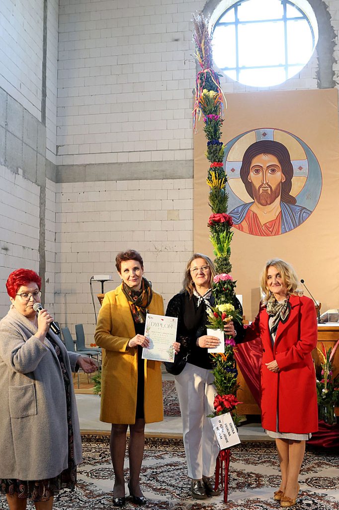 Na ilustracji znajdują się cztery osoby, które zawierają składniki, które zawierają wysokie, niebezpieczne narzędzie. Jeden z uczestników trzyma mikrofon, dwie osoby dzierżą certyfikaty, a w tle jest ikona religijna.