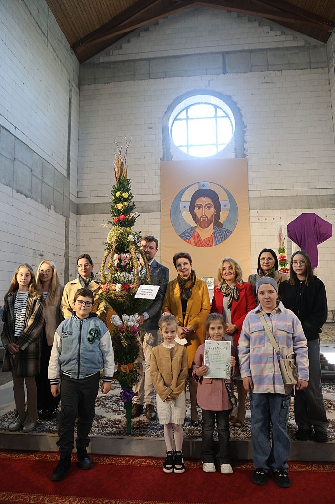 Na obrazku grupy ludzi, w tym dorośli i dzieci, którzy są dostępni, a obok nich znajdują się także ikony religijne. Wszyscy uczestnicy wyglądają na zadowolonych, co uroczystą lub świąteczną funkcję.