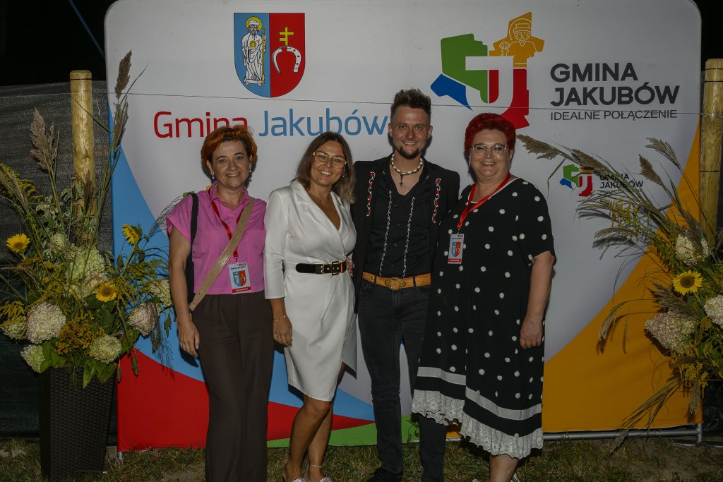 Cztery osoby stoją przed kolorowym, oficjalnym banerem Gminy Jakubów, ozdobionym kwiatami.