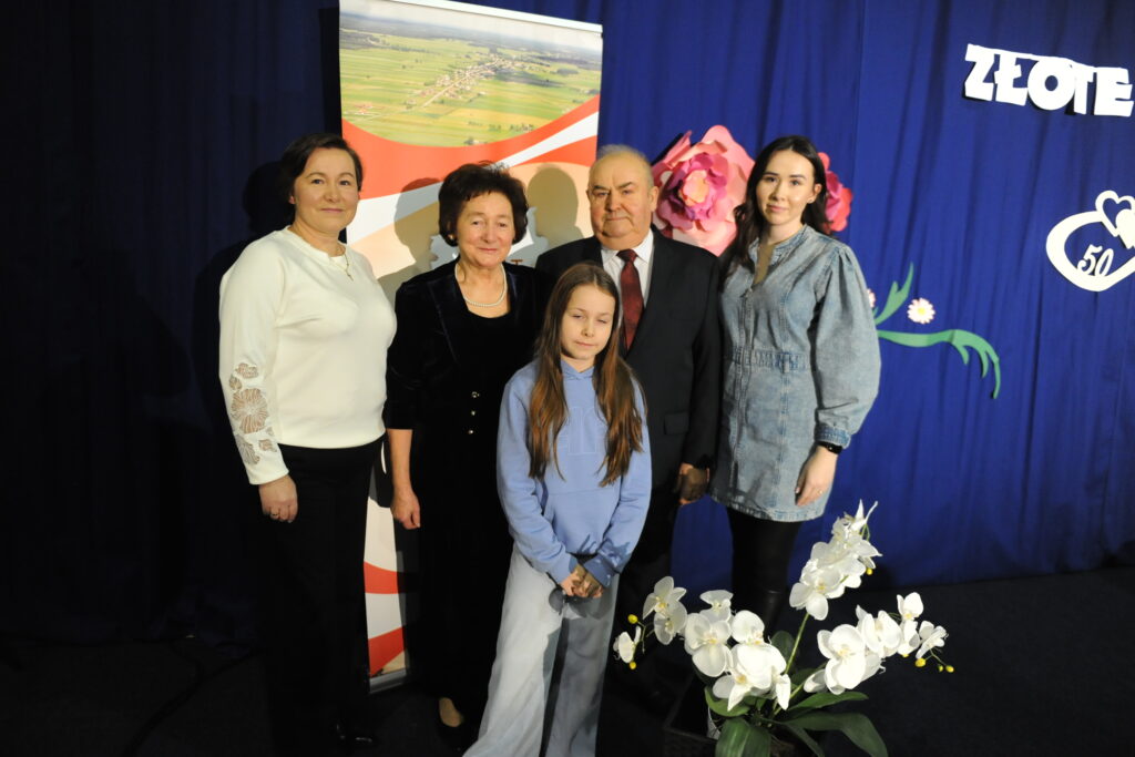 Na zdjęciu widać pięć osób na tle niebieskiej dekoracji, obok białych orchidei. Osoby są w eleganckich ubraniach. W tle jest także napis ZŁOTE i kwiatowe wzory.