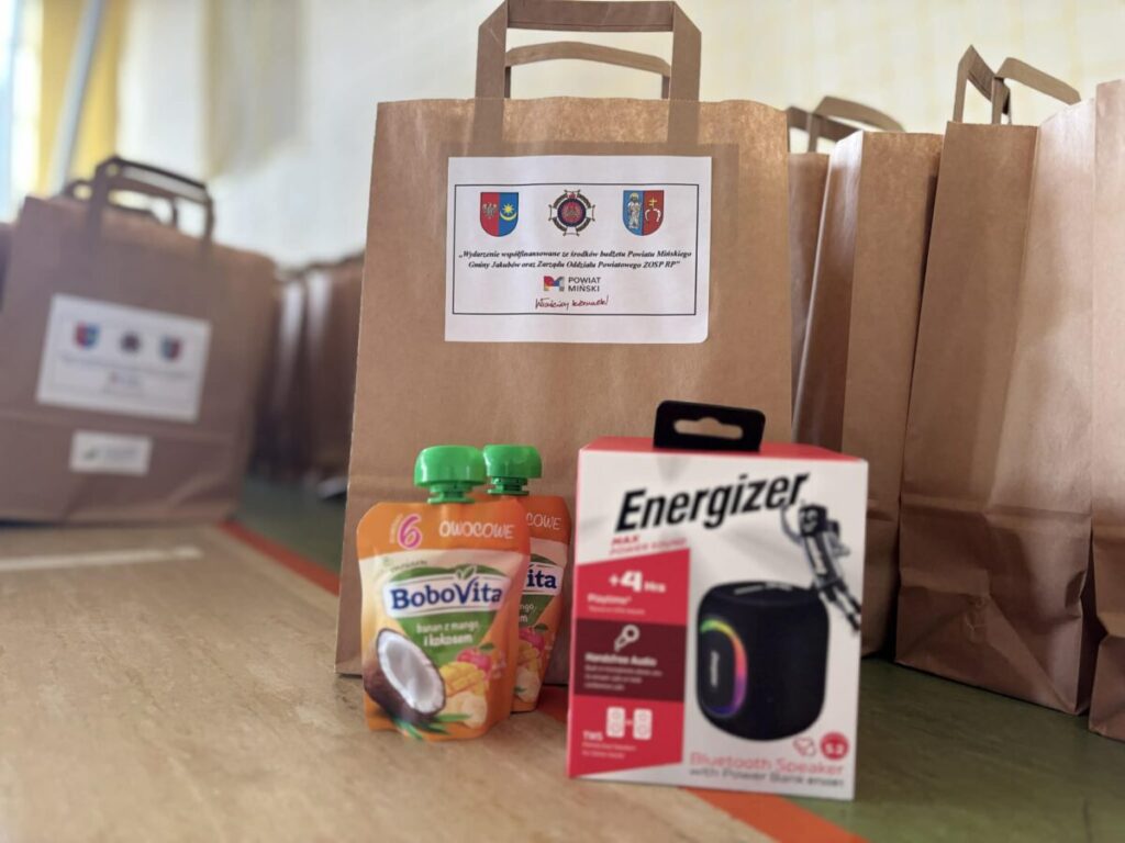 Na zdjęciu brązowe torby papierowe z logo oraz opakowania BoboVita i głośnik Energizer. Tło rozmyte, kolorystyka ciepła.