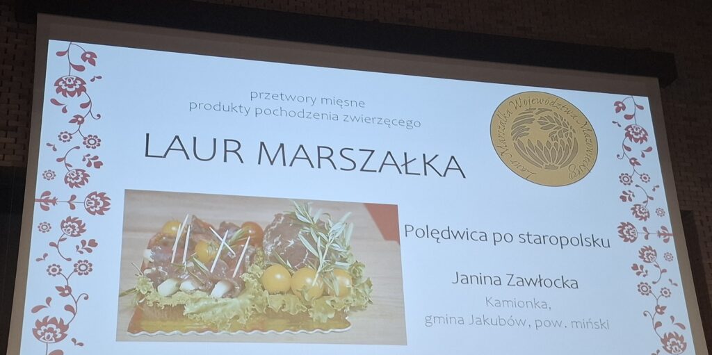 Plansza z nagrodą „Laur Marszałka” dla wyrobu mięsnego. Zdjęcie potrawy na tle dekoracji z czerwonymi wzorami kwiatowymi. Po prawej herb i szczegóły miejsca pochodzenia.
