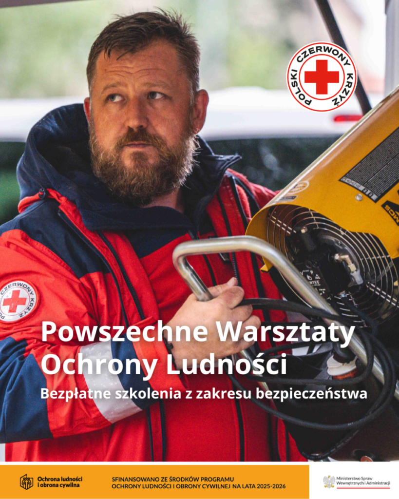 Mężczyzna w czerwonej kurtce trzyma żółte urządzenie. W tle rozmyty zielony krajobraz. Widoczne logo Polskiego Czerwonego Krzyża.